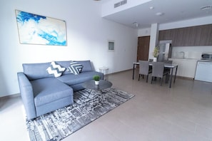 A modern living room with a grey sofa, a small round table, and a patterned rug. - HAPPY SEASON I Park Heights 2 Dubai Hills 1BR  (Dubai)