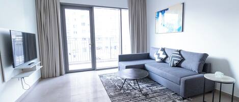 A modern living room with a grey sofa, a flat-screen TV, a round coffee table, and a patterned rug.