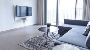 Una sala de estar moderna con un televisor de pantalla plana montado en la pared, un sofá gris, una pequeña mesa redonda de centro con una planta en maceta y una alfombra estampada.