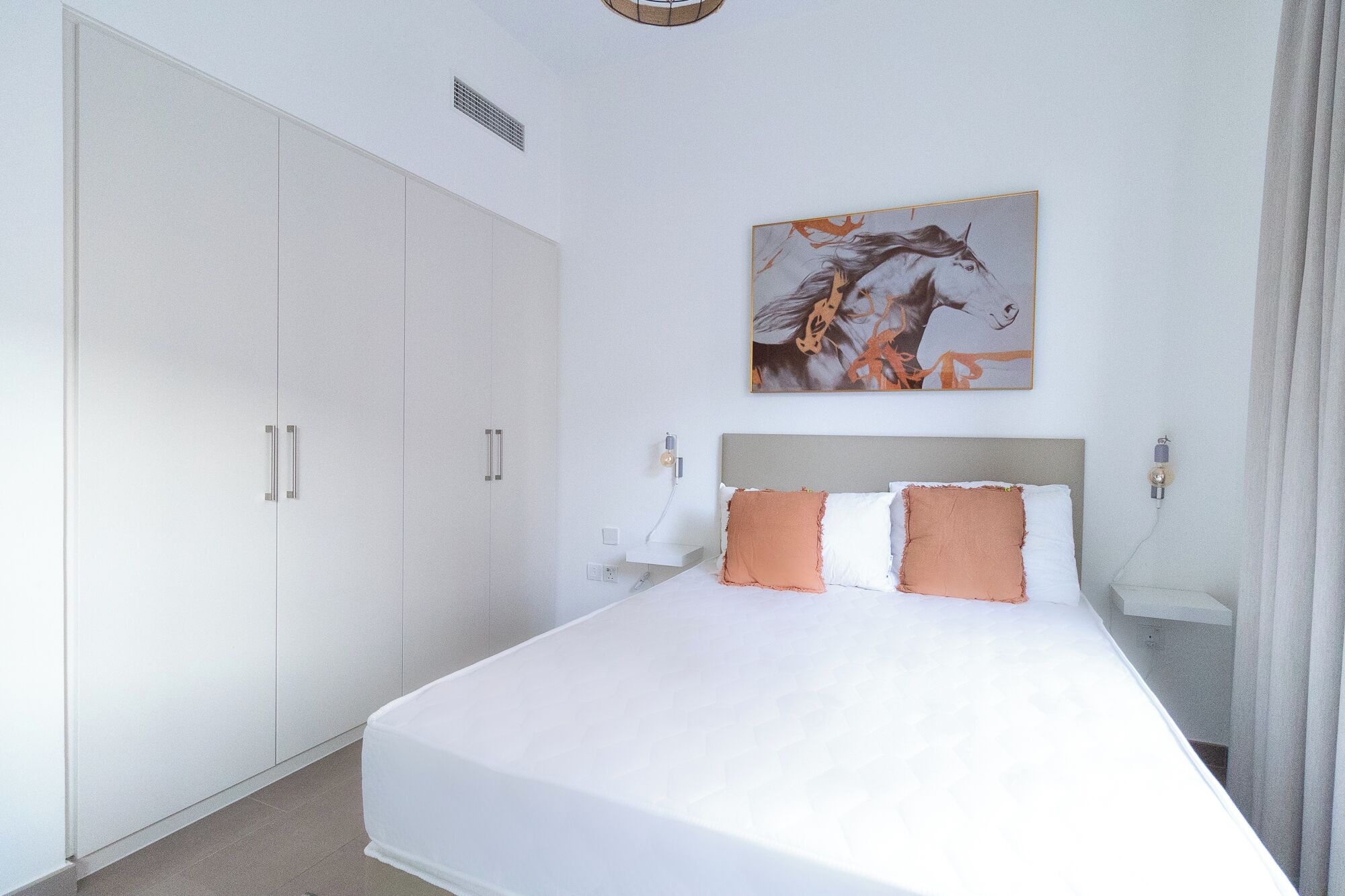 A bedroom with a large bed, white wardrobe, and a painting on the wall.