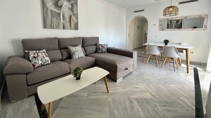 Un soggiorno moderno con un divano angolare grigio, un tavolino da caffè bianco e un'area pranzo con un tavolo bianco e sedie grigie.