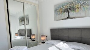 Una camera d'hotel moderna con un letto grande, una testiera grigia, lampade sui comodini, uno specchio e un quadro di un albero.