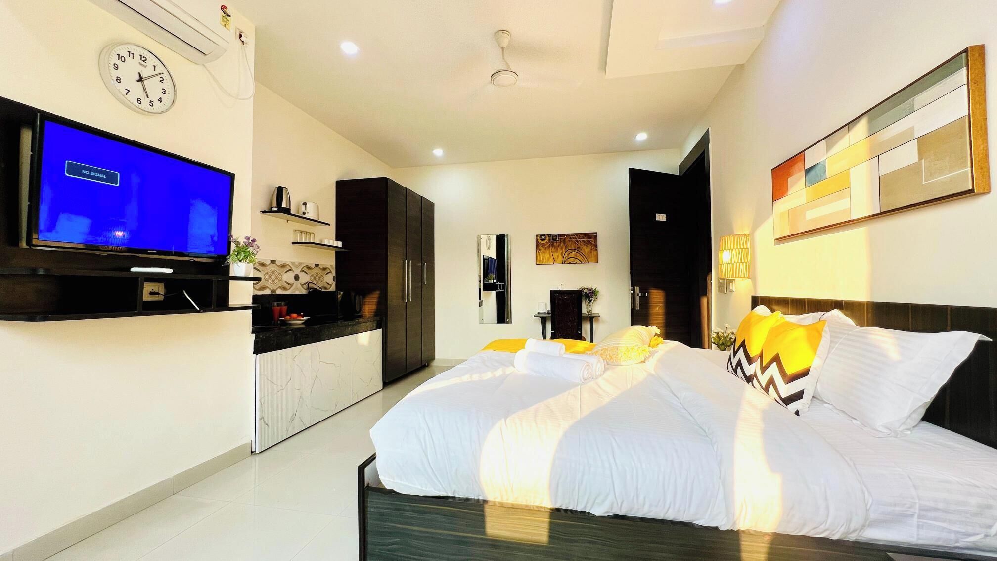 A modern hotel room with a large bed, a television, a kitchen area, and a bathroom.