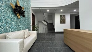 A modern reception area with a white sofa, a wooden reception desk, a staircase, and a wall with a blue marble-like pattern. - Bluo Stays - DLF Cybercity (Gurugram)
