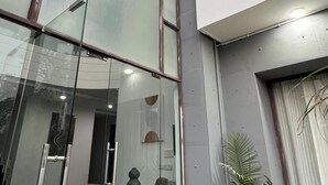 A modern building with large windows, a reception desk, and a green artificial turf area. - Bluo Stays - DLF Cybercity (Gurugram)