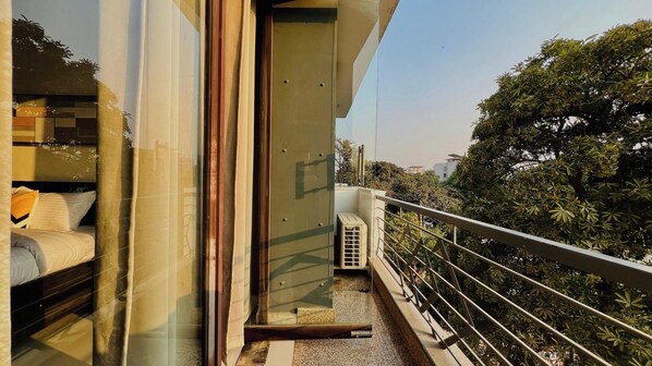 A balcony with a metal railing, a glass door, and a view of trees and buildings. - Bluo Stays - DLF Cybercity (Gurugram)