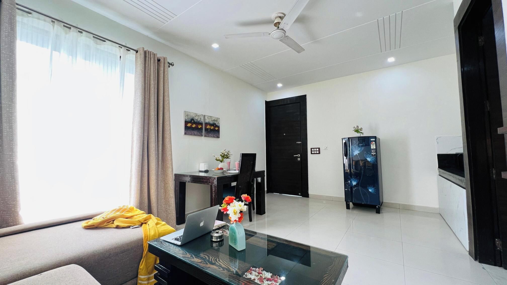 A modern living room with a sofa, a glass coffee table, a laptop, and a refrigerator.