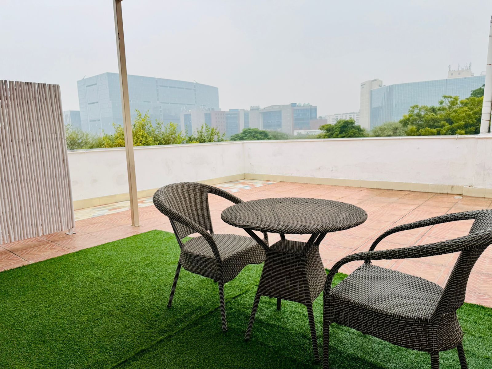 A rooftop terrace with two wicker chairs and a small round table, surrounded by artificial green grass.