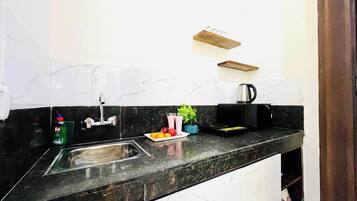 Una cocina con salpicadero de mármol, un lavamanos de acero inoxidable, una cafetera y un frutero.