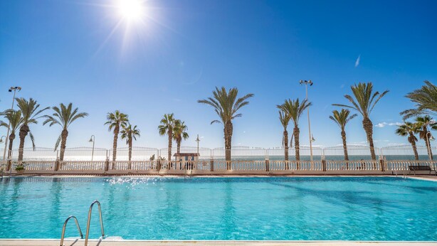Una piscina con cerca blanca, palmeras y farolas.
