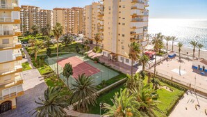 Un edificio residencial alto con varios balcones, cancha de tenis y vista al mar.