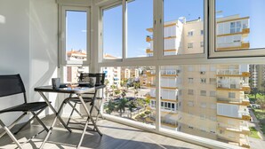 Un balcón con mesa y sillas, ventanas amplias y vistas de edificios circundantes.