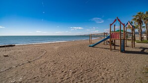 Una playa con una estructura de juegos, que incluye un tobogán y una zona de escalada, y palmeras al fondo.
