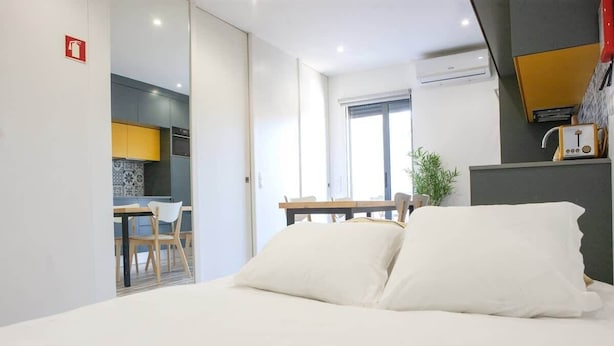 Moderni hotellihuone, jossa on sänky, ruokailutila ja avoimesta ovesta näkyvä keittiö.