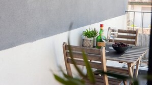 Un balcon avec une table en bois, un panier de fruits, une bouteille de vin et un verre d’eau.