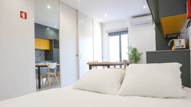 Une chambre d’hôtel moderne comprenant un lit, un coin repas et une cuisine visible à travers une porte ouverte.