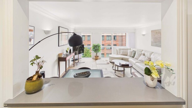 A modern living room with a sofa, coffee table, and a view of a building through large windows.