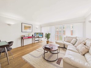 Una sala moderna con un sofá, una mesa de centro y un televisor. Hay un comedor con una mesa y sillas.