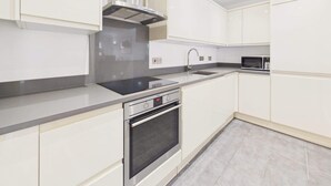 A modern kitchen with white cabinetry, a stainless steel range hood, a built-in oven, and a microwave.