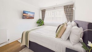 A bedroom with a bed, a television, and a window with curtains.