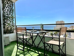 A balcony with a table and chairs, a glass of wine, and a view of the sea and buildings. - Charming Boho Apartment with Pool and Terrace in Torremolinos (Torremolinos)