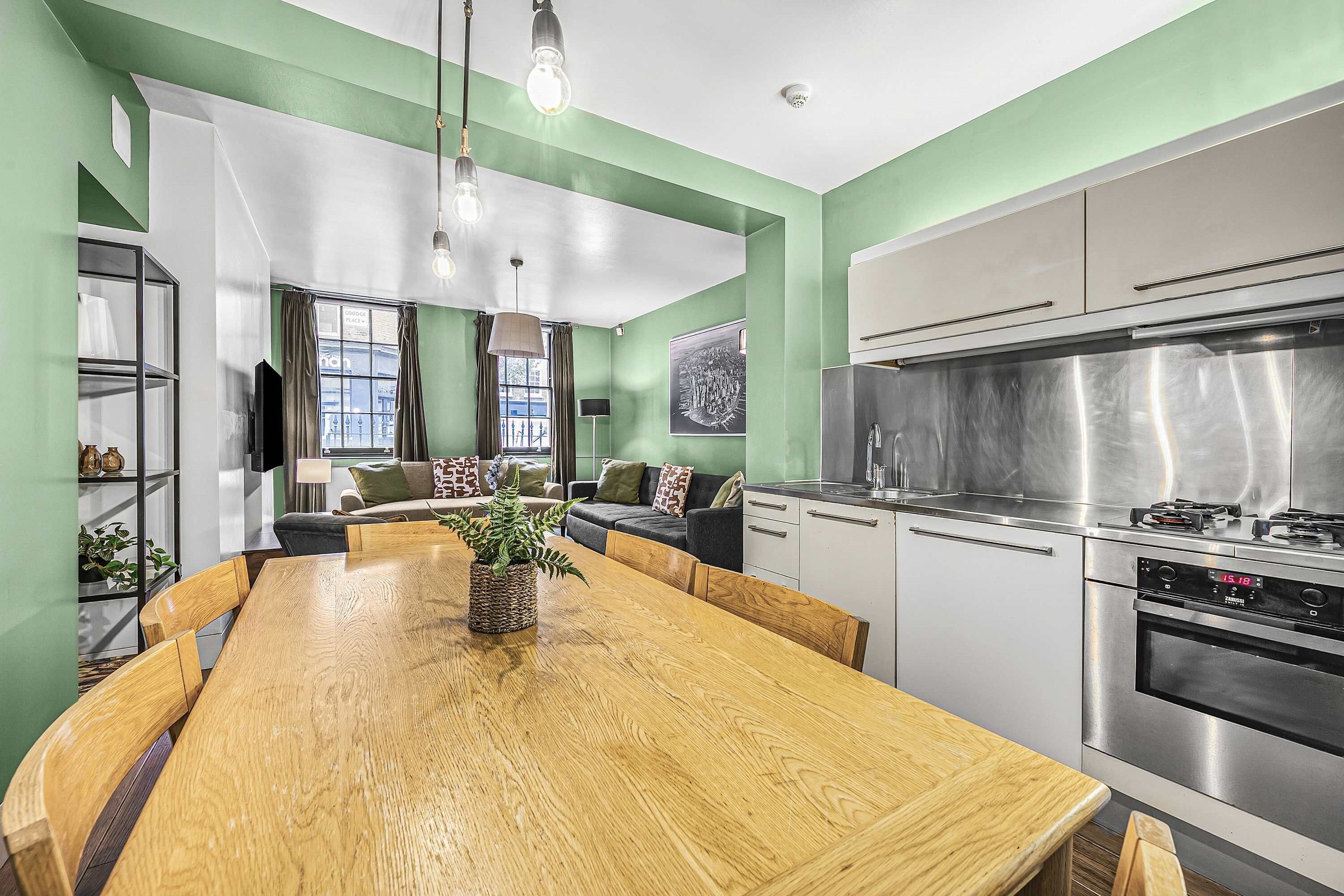 Una cocina moderna con electrodomésticos de acero inoxidable, una mesa de comedor de madera y un área de estar con sofá y televisor.