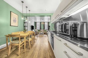 A modern kitchen with a dining area, wooden flooring, and a green wall.
