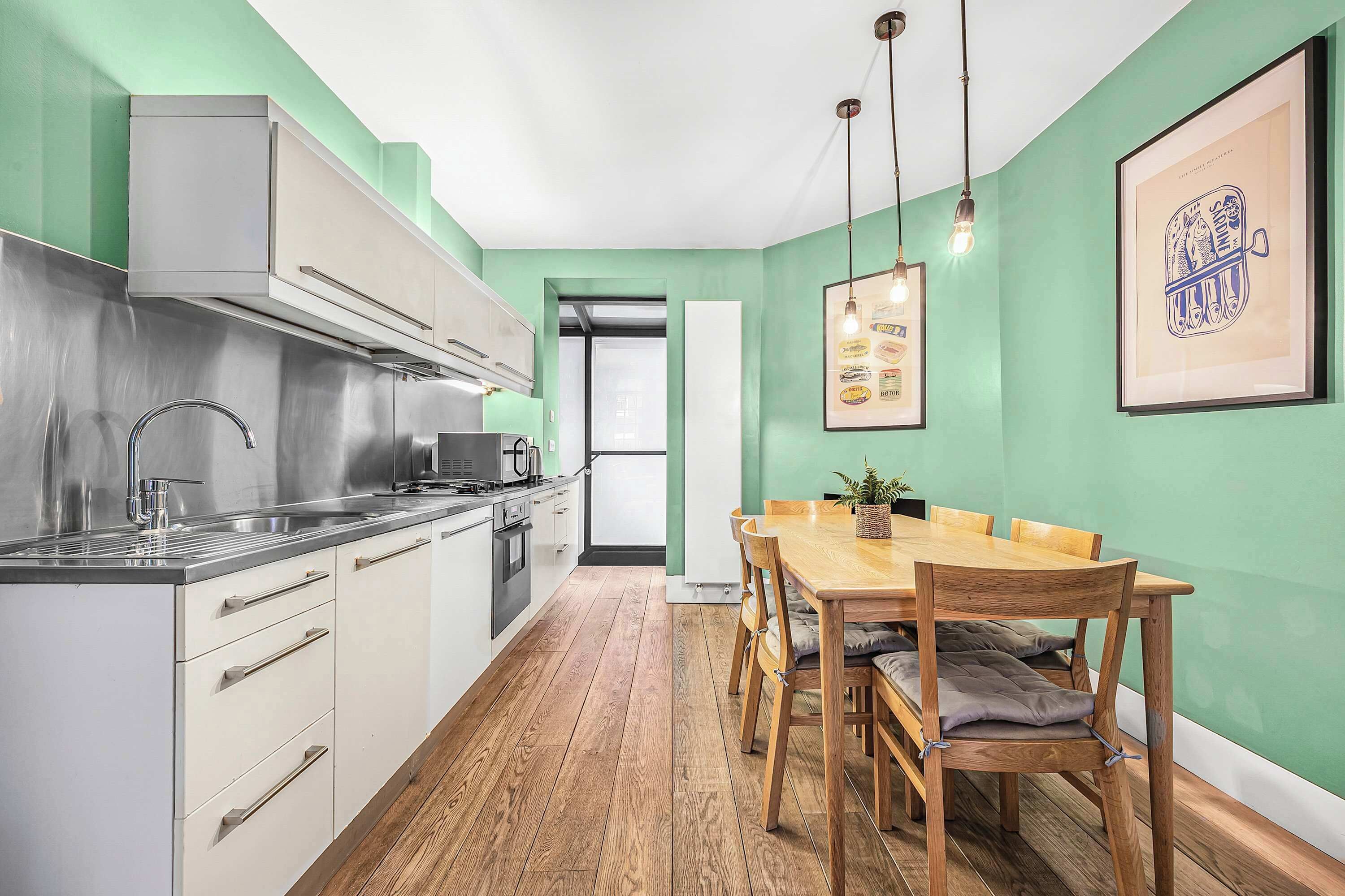 Una cocina moderna con electrodomésticos de acero inoxidable, una mesa de comedor de madera con sillas y una pared verde.