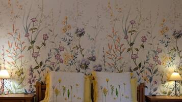 A bedroom with floral wallpaper, a bed with two pillows, and bedside tables with lamps.