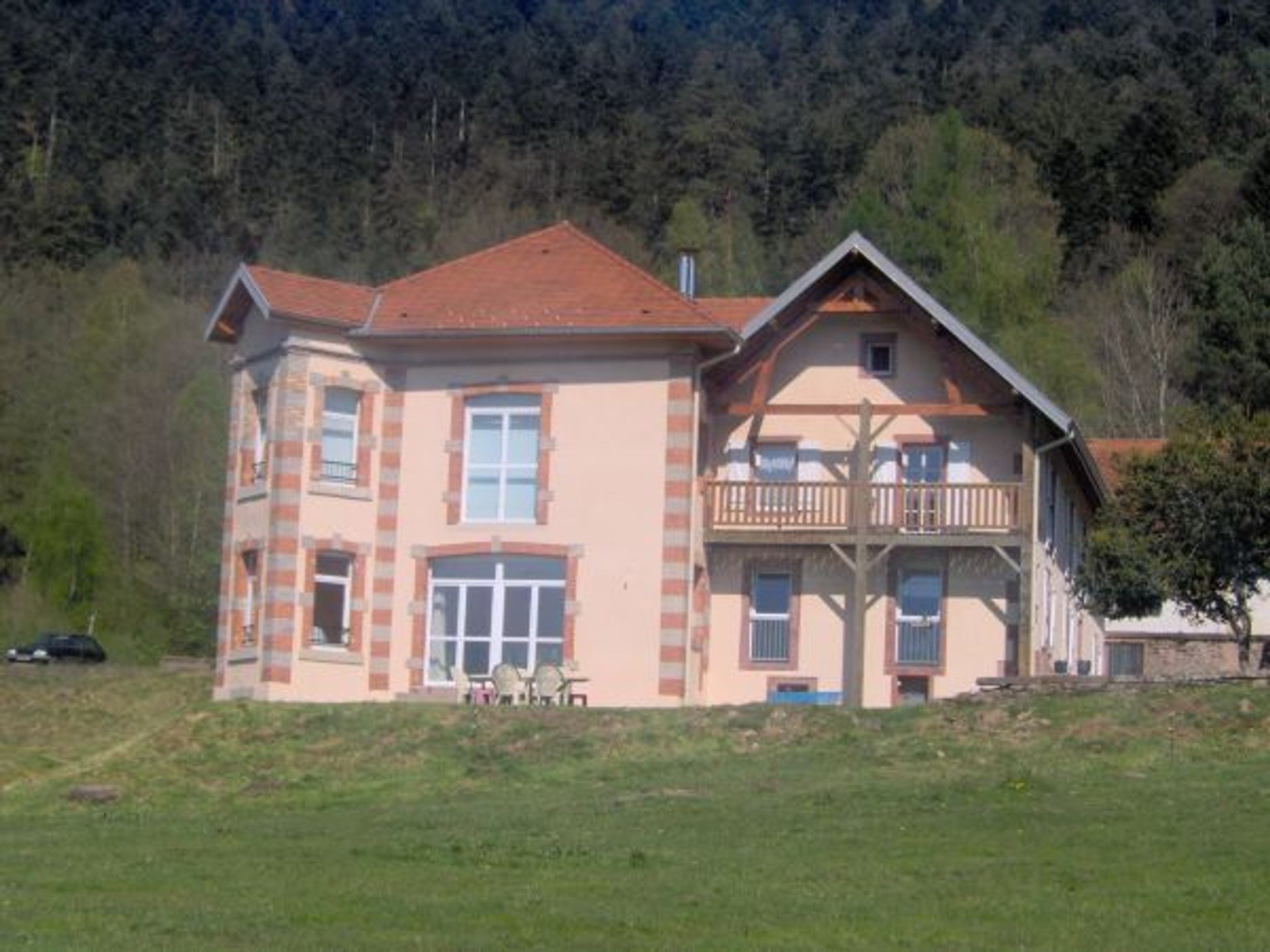 Une maison à deux étages dotée d’un balcon, d’un toit recouvert de tuiles rouges et d’un petit porche.