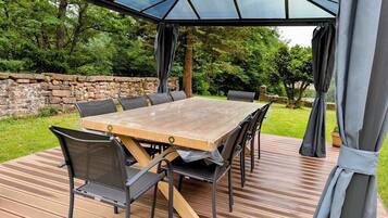 Un patio al aire libre con una mesa y sillas de madera, una cubierta de vidrio y un muro de piedra de fondo.