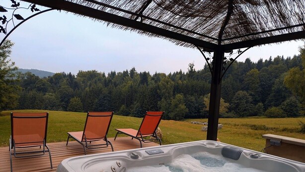 Un jacuzzi con tres sillas en una terraza de madera, con vistas a un paisaje boscoso.