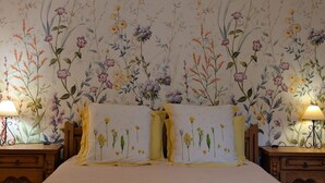 Un dormitorio con papel tapiz floral, una cama con dos almohadas y mesitas de noche con lámparas.