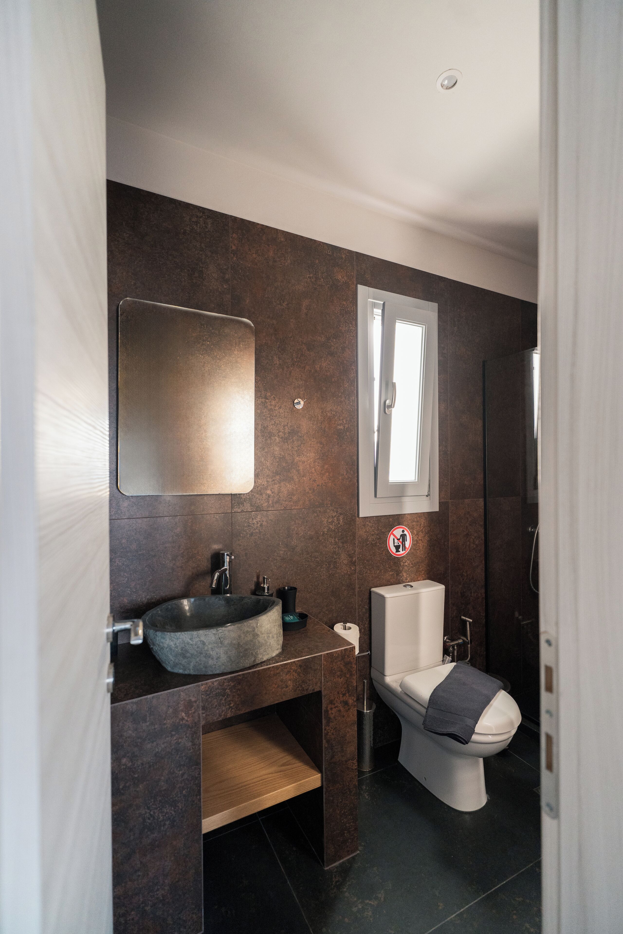 A modern bathroom with a stone sink, a toilet, and a large mirror.