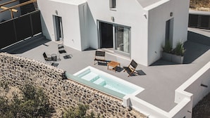 Una casa moderna con piscina, mobiliario exterior y un muro de piedra.