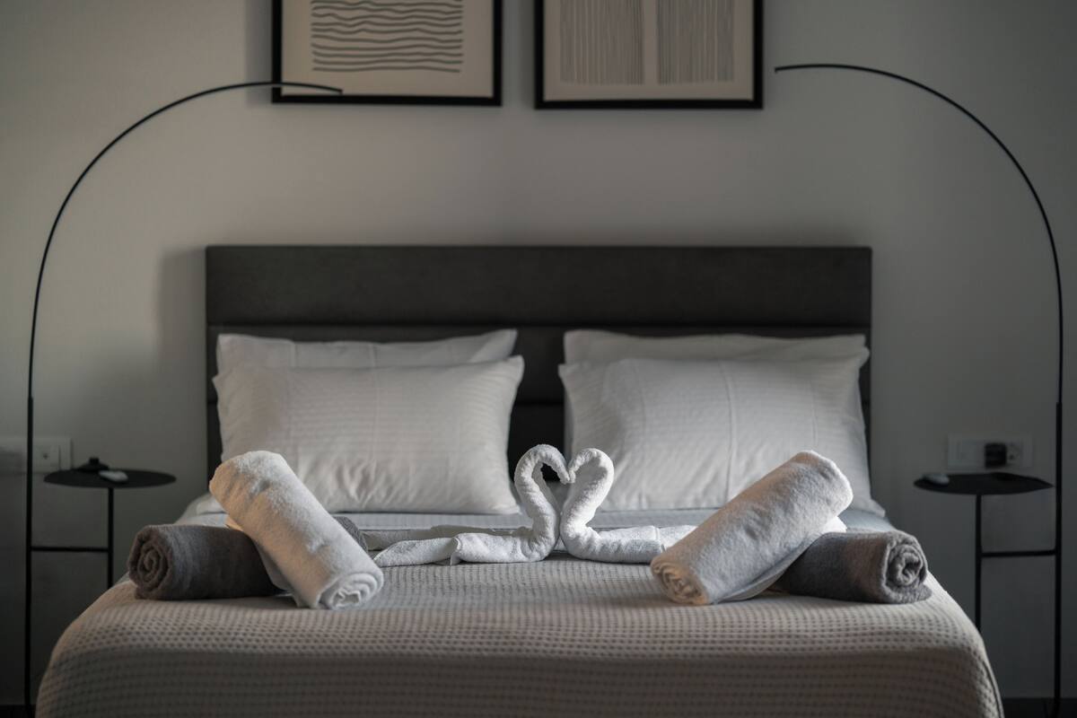 Una cama bien hecha con sábanas blancas y dos toallas dispuestas en forma de corazón.