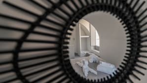 Un espejo circular de marco negro que refleja una habitación con cama, toalla y puerta.