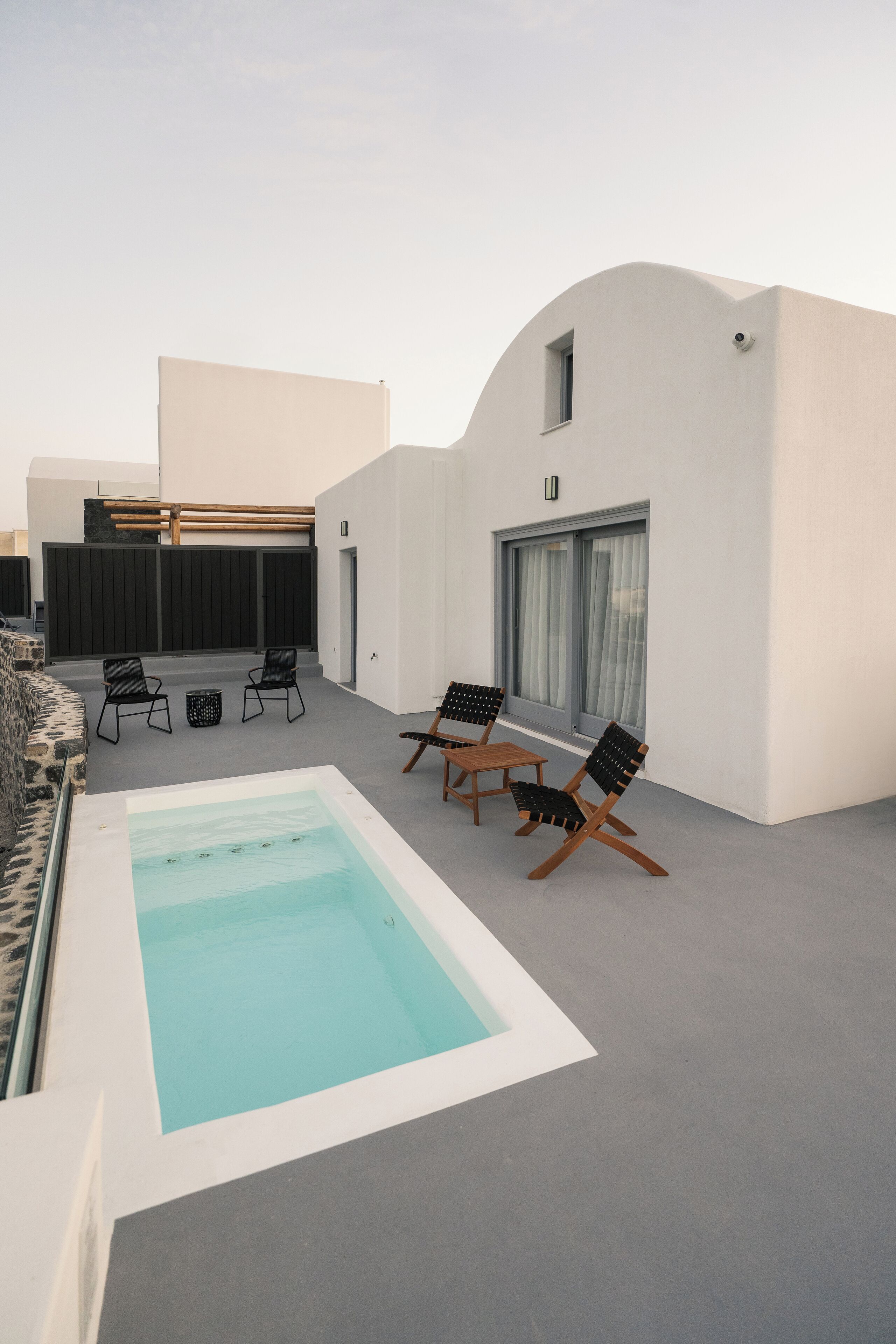 A modern outdoor pool area with a rectangular pool, black lounge chairs, and a stone wall.