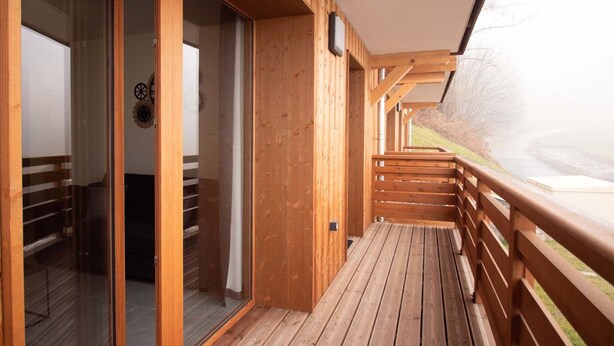 A wooden deck with a glass door leading to a room, a wooden railing, and a view of a landscape. - New T2 Apartment with balcony, covered parking, 4 guests. (Valmorel)