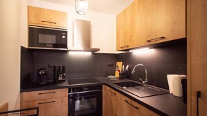 A modern kitchen with wooden cabinets, a black countertop, a built-in oven, a microwave, a coffee maker, and a sink. - New T2 Apartment with balcony, covered parking, 4 guests. (Valmorel)
