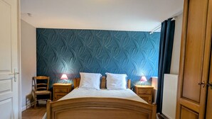 A bedroom with a wooden bed, two bedside tables with lamps, a chair, and a blue patterned wall. - Iris Room in renovated house amidst nature (Moyenmoutier)