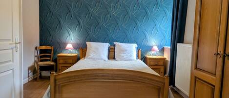 A bedroom with a wooden bed, two bedside tables with lamps, a chair, and a blue patterned wall.