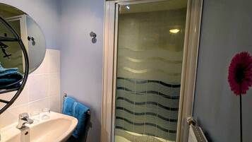 A bathroom with a sink, mirror, towel rack, shower with frosted glass, and a radiator.