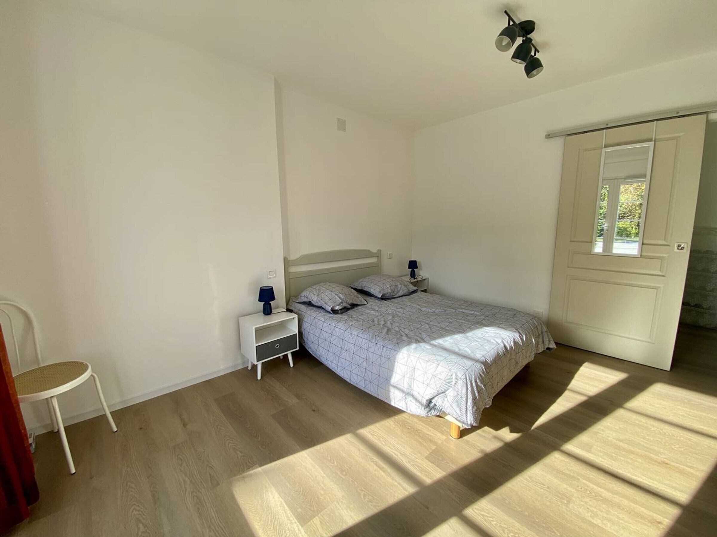 Une chambre à coucher avec un lit, des tables de chevet, une chaise et une porte avec une fenêtre.