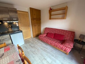 Un espacio habitable compacto con kitchenette, un sofá con cojines estampados, una mesa de comedor con sillas y una pequeña mesita auxiliar.
