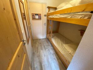 Un pasillo estrecho con una puerta de madera y una litera con ropa de cama blanca.