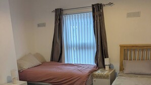 Ein Schlafzimmer mit zwei Betten, einem Nachttisch mit Lampe, einem Fenster mit Vorhängen und einer Heizung.