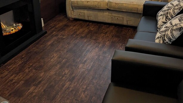 Ein Wohnzimmer mit einem beigefarbenen Sofa, zwei gemusterten Kissen, einem dunkelholzigen Couchtisch und einem Kamin mit Steinverkleidung.
