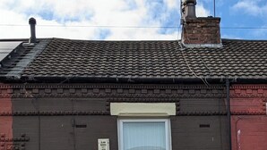 Ein zweistöckiges Wohngebäude mit dunkelbrauner Fassade, einem Erkerfenster mit weißem Rahmen und einer roten Tür.