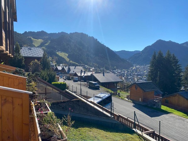 A mountain village with traditional wooden houses, a paved street, and a clear view of the surrounding hills.